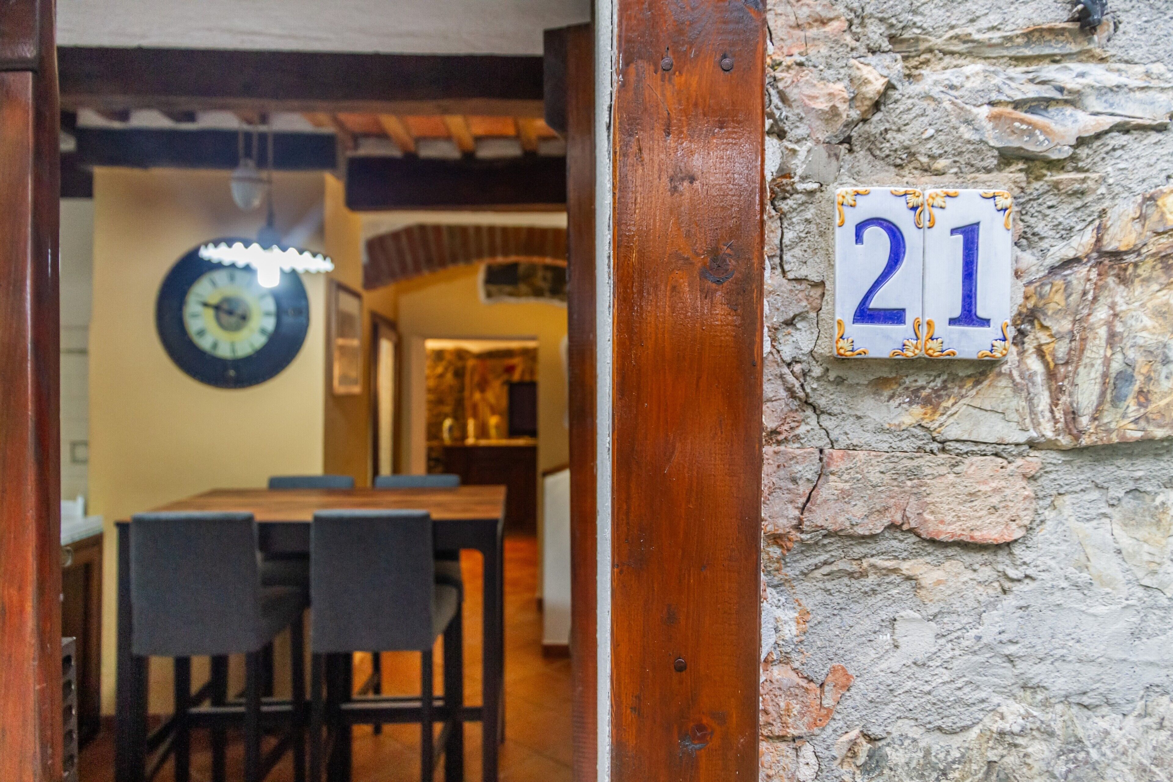 A wooden door frame, a stone wall with a number plaque, and a dining area with chairs and a table.