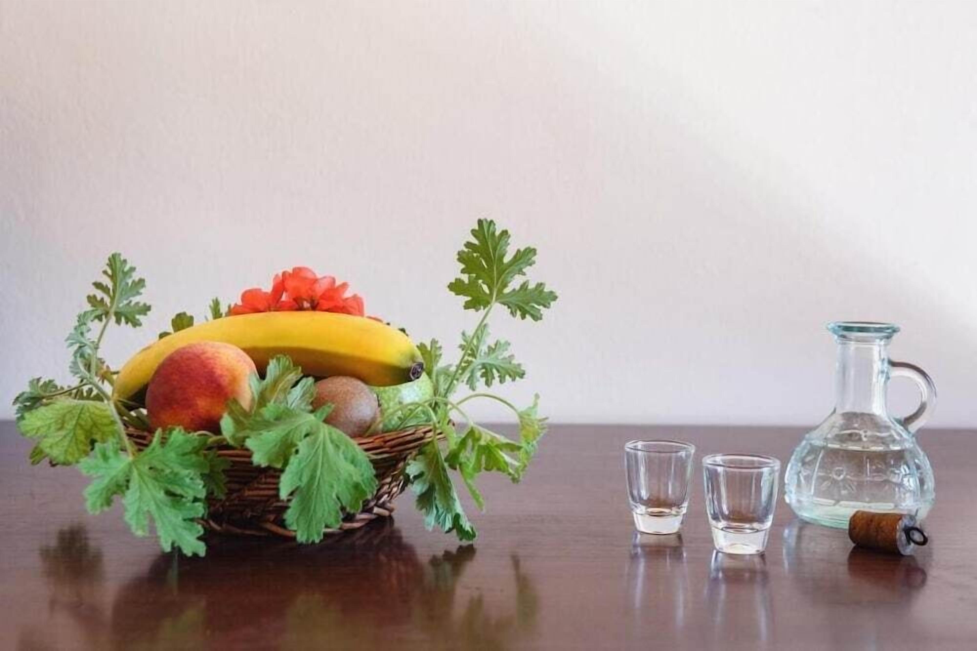 Un panier en osier rempli de fruits et une carafe en verre posés sur une table en bois.