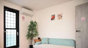 Ein Zimmer mit einem Bett, einer Topfpflanze, einer Wandklimaanlage und zwei Wandbildern.
