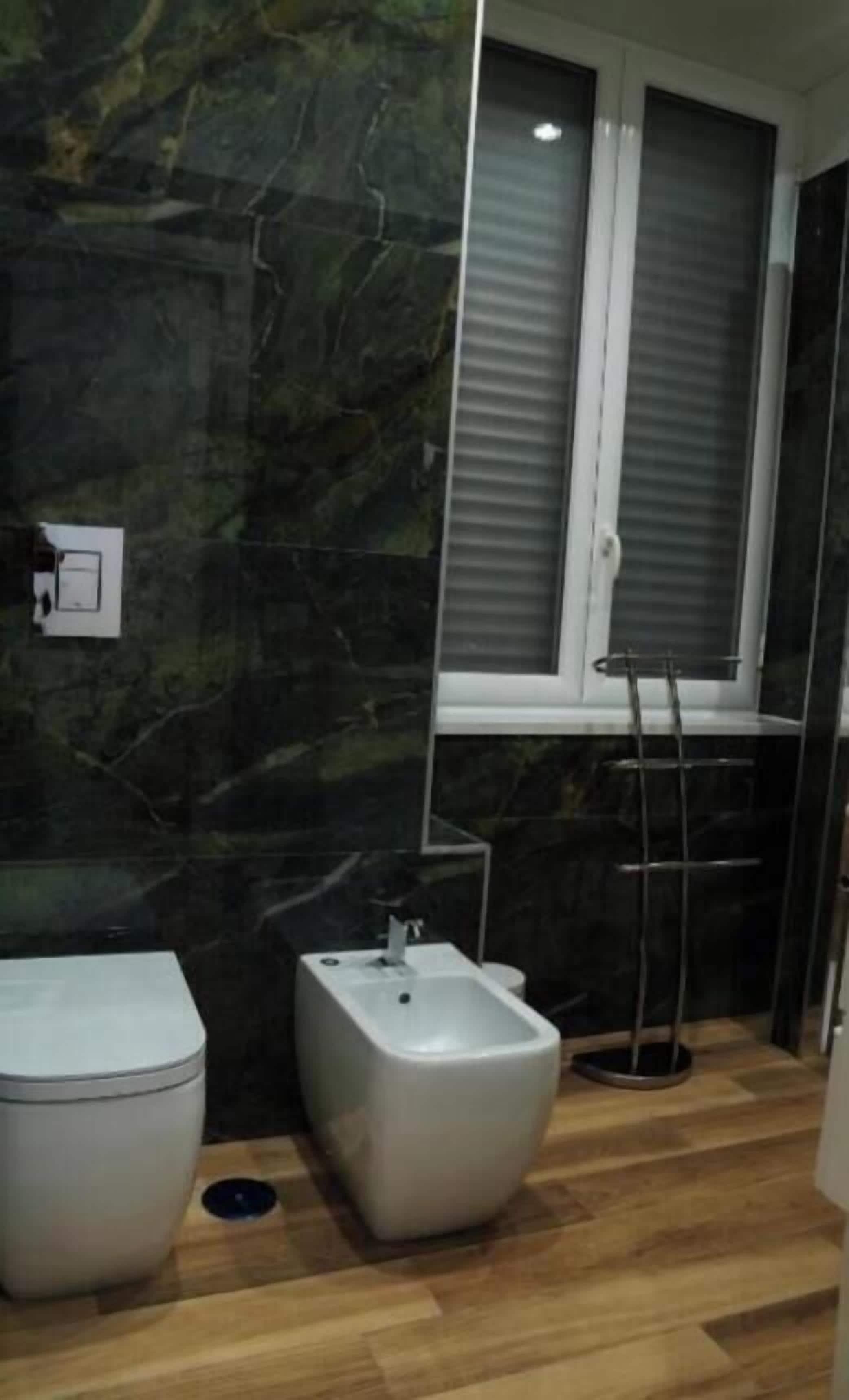A bathroom with a toilet, bidet, and a window with blinds.
