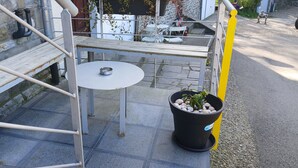 Un’area patio con un tavolo rotondo e panche, una pianta in vaso decorata con conchiglie, e un muro in pietra sullo sfondo.