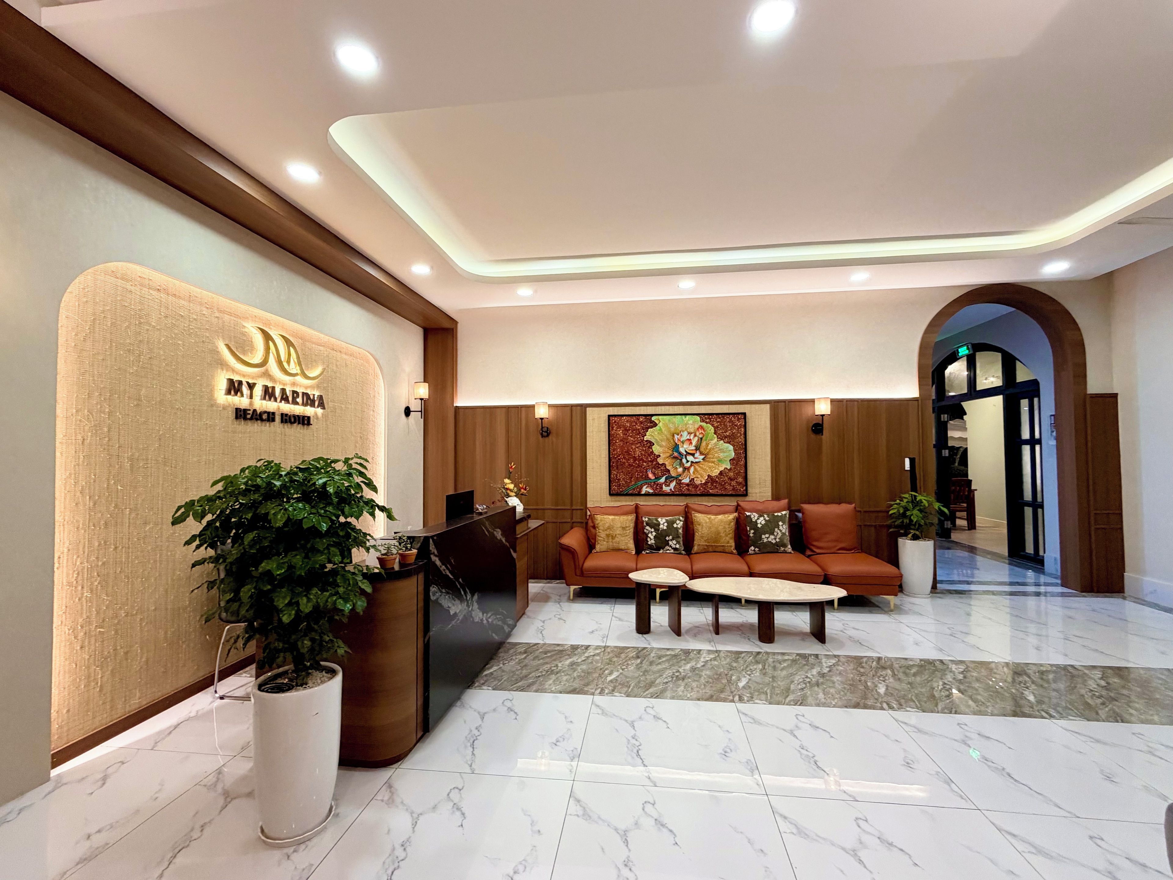 A hotel reception area with a reception desk, a seating area, and a large painting on the wall.