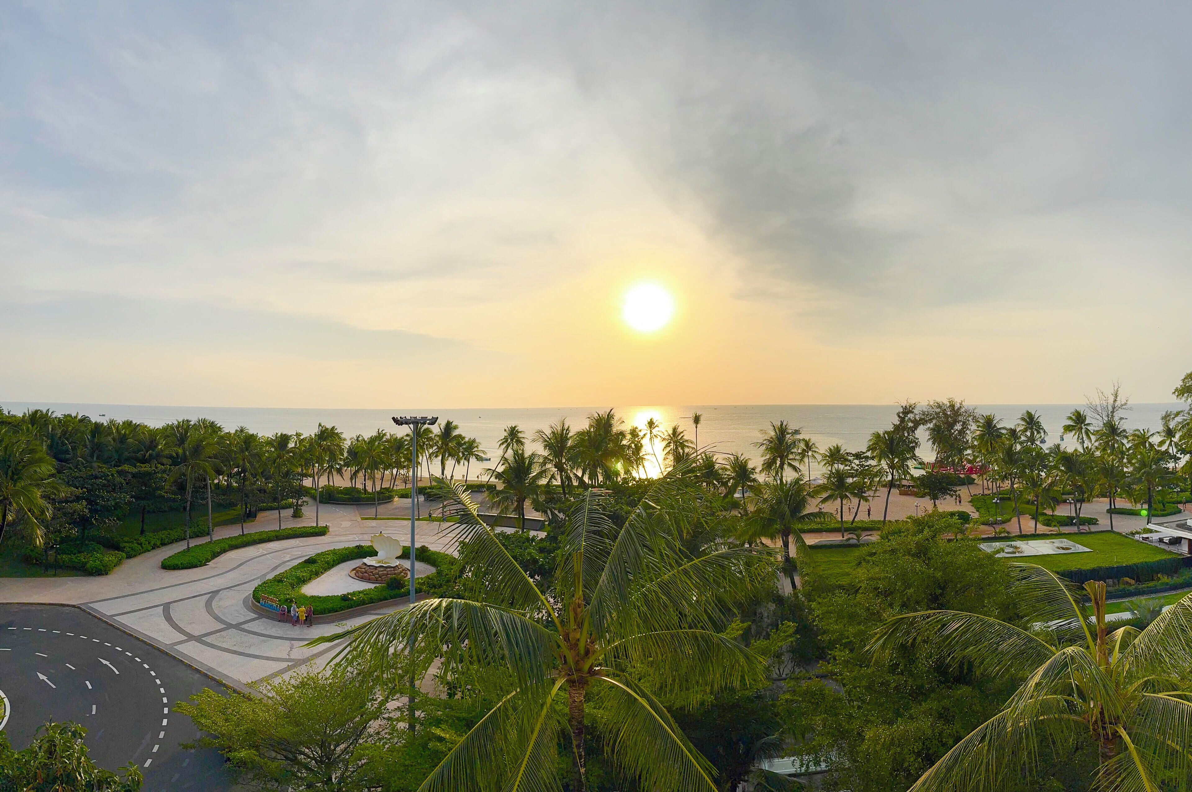A coastal resort with a roundabout, palm trees, and a view of the sea.