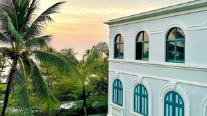 A white building with arched windows and balconies, surrounded by lush greenery and palm trees. - My Marina Beach Hotel Phu Quoc (Phu Quoc)