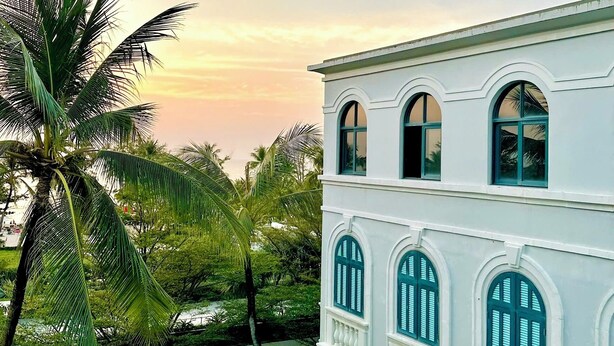 A white building with arched windows and balconies, surrounded by lush greenery and palm trees. - My Marina Beach Hotel Phu Quoc (Phu Quoc)