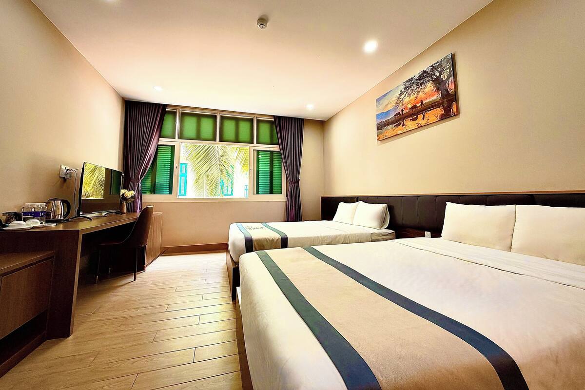 A hotel room with two beds, a desk with a computer, a window with curtains, and a painting on the wall.