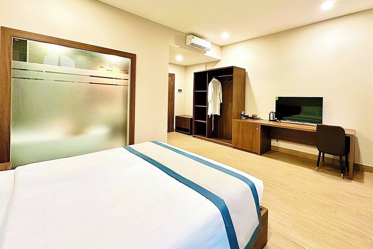 A hotel room with a bed, a desk, a TV, a wardrobe, and an air conditioning unit.