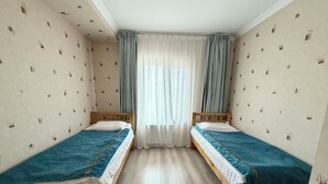 A room with two wooden beds, a window with curtains, and patterned wallpaper. - 30 Convenient Central 2BR Apartment (Ulaanbaatar)