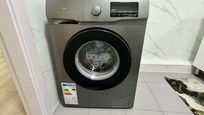 A front-loading washing machine with a control panel, placed in a bathroom with white marble tiles. - 30 Convenient Central 2BR Apartment (Ulaanbaatar)