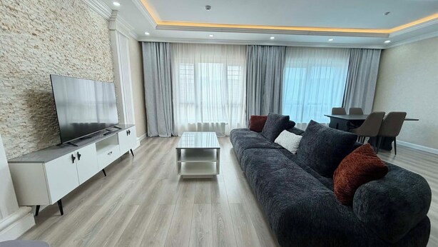 A modern living room with a flat-screen TV, a dark sofa, a coffee table, and a dining area with chairs. - 30 Convenient Central 2BR Apartment (Ulaanbaatar)