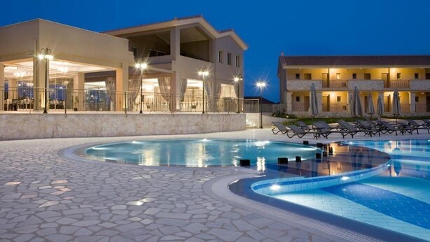 Un hotel con piscina, mobiliario exterior y fachada luminosa.