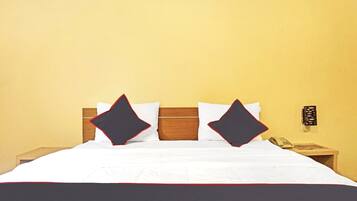 A hotel room with a bed, two pillows, a bedside table with a telephone, and a wall-mounted light fixture.