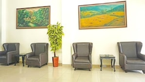 Une salle d’attente comprenant quatre fauteuils en cuir, deux tableaux, une plante en pot et une petite table.
