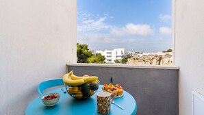 Un balcon avec une table préparée pour le petit-déjeuner, comprenant un saladier de fruits, un panier de bananes et une tasse.