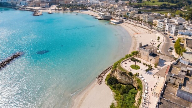 Une vue aérienne d’une ville côtière, avec une plage, des bâtiments et une mer bleue et limpide.