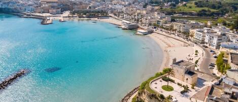 An aerial view of a coastal city with a beach, buildings, and a clear blue sea.