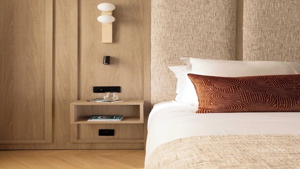 A hotel room with a wooden wardrobe, a bedside table with a lamp, a bed with patterned pillows, and a textured headboard. - Design Apartment a/c 1BR/4P - Saint-Germain (Paris)