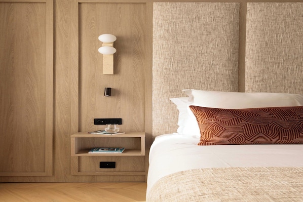 A hotel room with a wooden wardrobe, a bedside table with a lamp, a bed with patterned pillows, and a textured headboard. - Design Apartment a/c 1BR/4P - Saint-Germain (Paris)