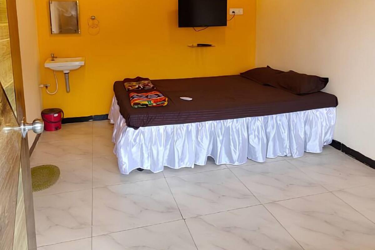A bedroom with a bed, a ceiling fan, an air conditioning unit, a television, a sink, and a mirror.