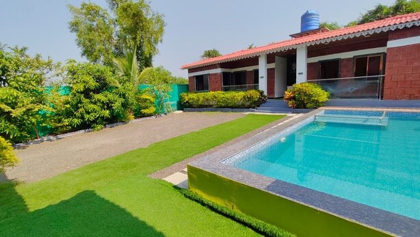 A swimming pool, a building with a red roof, and a well-maintained lawn. - Maitri Resort (Alibag)