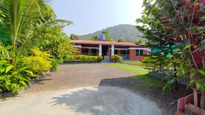 A building with a red roof, surrounded by greenery and a gravel driveway. - Maitri Resort (Alibag)