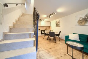 A staircase leading to a dining area with a round table and chairs, a green sofa, and a wall-mounted artwork. - Apartment Veris in the heart of the old town of Vrbnik (Vrbnik)