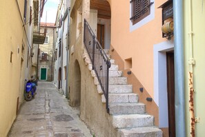 A narrow street with stone steps leading to a building with a wooden door and a metal railing. - Apartment Veris in the heart of the old town of Vrbnik (Vrbnik)