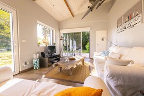 Una sala de estar moderna con un sofá, una mesa de centro y una televisión. Hay un ventanal y una puerta que da al exterior.