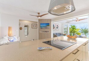 A modern kitchen with a central island, a ceiling fan, and a view of the ocean through large windows. - Quatre Vents (Sainte-Luce)