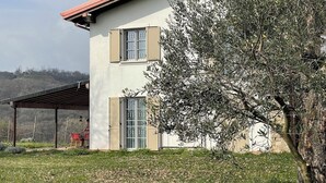 Ein zweigeschossiges Haus mit einer überdachten Terrasse, einem Baum im Vorgarten und Blick auf die Landschaft.