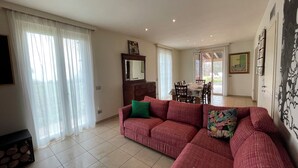 A living room with a sofa, a dining table, and a view through a glass door. - Lake View Country Glam House "SAN MARTINE" (2+2+1+3 guests) Family Villa for up to 8 guests (Lombardia)