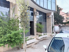 A modern building with large windows, air conditioning units, and a small tree in the foreground. - 2 Cozy 1-bedroom apartments in  Tirana (tirana)