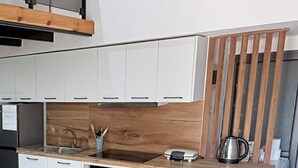Moderni keittiö, jossa on valkoiset kaapit, puinen työtaso, sisäänrakennettu uuni ja seinälle kiinnitetty hylly.