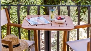 Een balkon met een tafel, stoelen, een hoed en een schaal met fruit.