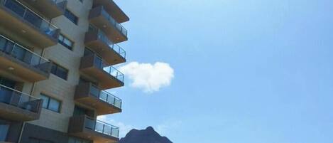Un hotel de varios pisos con balcones, un paisaje de montañas al fondo y un cielo despejado.