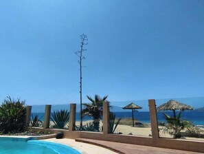A pool with a view of the beach and ocean, surrounded by palm trees and a wooden deck.
