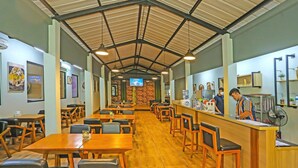 Un restaurant avec des tables et des chaises en bois, un comptoir où se tient un serveur, et un téléviseur accroché au mur.