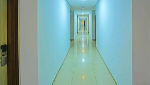 Un long couloir étroit, avec une rangée de portes d’un côté et un plancher de couleur claire.