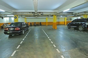 A multi-level parking garage with cars parked on different levels, visible structural beams, and a ceiling with exposed pipes.