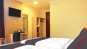 Habitación de hotel con dos camas, televisor montado en la pared, escritorio con silla y armario.