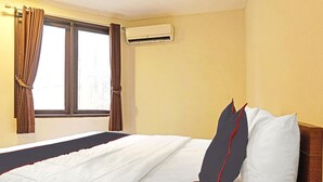 Een hotelkamer met een bed, gordijnen, een airconditioning en een raam.