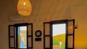 Ein Schlafzimmer mit Bett, zwei Fenstern mit geöffneten Fensterläden, einer Pendelleuchte und einer Heizung.