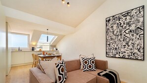 A modern interior with a sofa, geometric pillows, a dining area, and a kitchen. - Modern Studio for Easy Everyday Living (Lisbon)