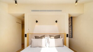 A bedroom with a bed, bedside lamps, a wall-mounted artwork, and a ceiling vent. - Modern Studio for Easy Everyday Living (Lisbon)