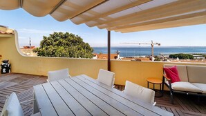 An outdoor patio with a table and chairs, a covered area, and a view of the sea and construction cranes. - Sunny Terrace Apartment w/ River Views (Lisbon)
