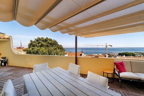 An outdoor patio with a table and chairs, a covered area, and a view of the sea and construction cranes. - Sunny Terrace Apartment w/ River Views (Lisbon)