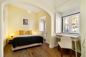 Un dormitorio con cama, mesitas de noche, escritorio, silla, ventana y lámpara colgante.