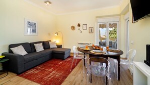 A living room with a sectional sofa, a dining table with chairs, a red rug, and a TV mounted on the wall. - Sunny Terrace Apartment w/ River Views (Lisbon)