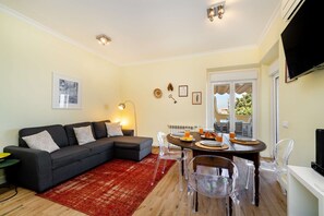 A living room with a sectional sofa, a dining table with chairs, a red rug, and a TV mounted on the wall. - Sunny Terrace Apartment w/ River Views (Lisbon)