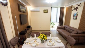 A dining area with a table set for four, a sofa, a television, and a wall-mounted air conditioner. - 3-bedroom Family Paradise Villa in Woods (Magnetiti)